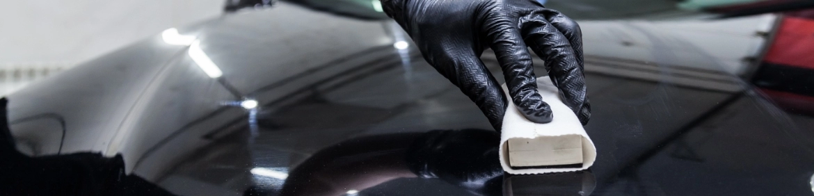 Dłoń w czarnej rękawiczce trzymająca biały przedmiot na masce pojazdu